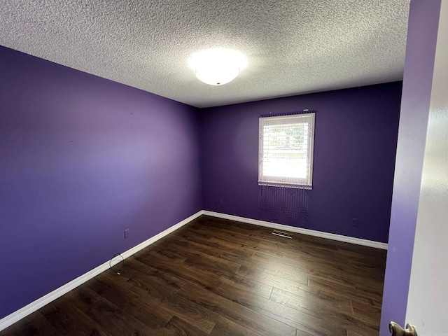 empty room with dark hardwood / wood-style floors and a textured ceiling