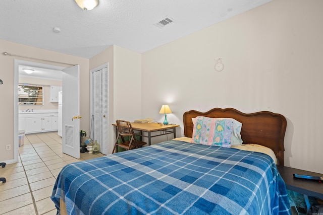 bedroom featuring a closet, sink, ensuite bathroom, light tile patterned floors, and a textured ceiling