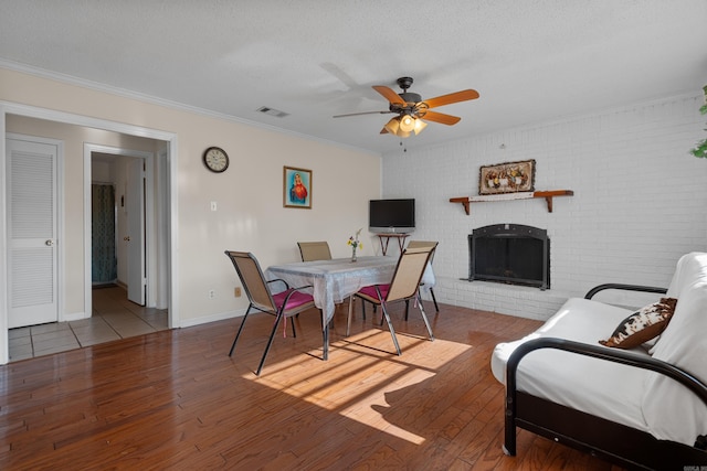 dining area with ceiling fan, ornamental molding, a brick fireplace, a textured ceiling, and light hardwood / wood-style floors