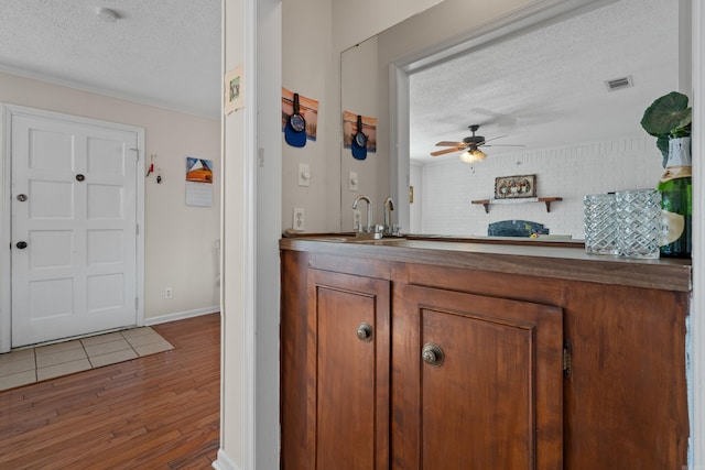 interior space with a ceiling fan, a textured ceiling, visible vents, wood finished floors, and baseboards
