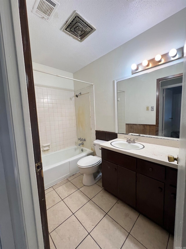 full bathroom with tile patterned flooring, toilet, tiled shower / bath combo, vanity, and a textured ceiling