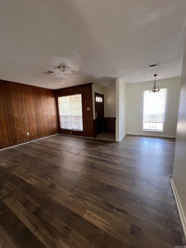 unfurnished living room with wood walls, plenty of natural light, and dark hardwood / wood-style flooring