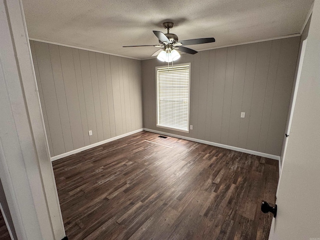 empty room with a textured ceiling, dark hardwood / wood-style flooring, wooden walls, and ceiling fan