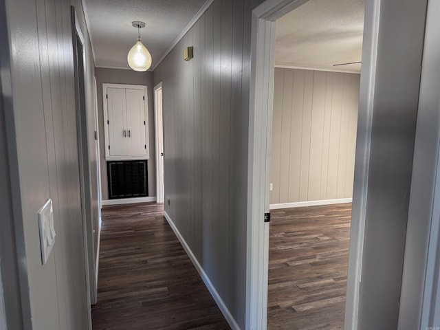 hall featuring a textured ceiling, wood walls, dark hardwood / wood-style flooring, and crown molding