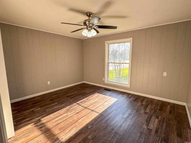 spare room featuring wood-type flooring, wood walls, ornamental molding, and ceiling fan