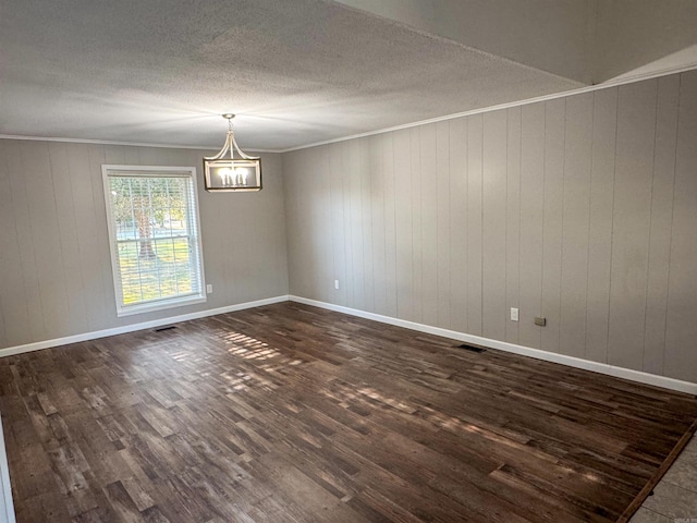 unfurnished room with ornamental molding, a textured ceiling, wooden walls, a chandelier, and dark hardwood / wood-style floors