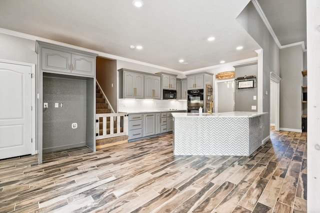 kitchen featuring wood-type flooring, gray cabinets, black appliances, and a center island