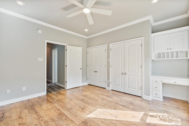 unfurnished bedroom featuring ceiling fan, built in desk, two closets, light hardwood / wood-style flooring, and ornamental molding