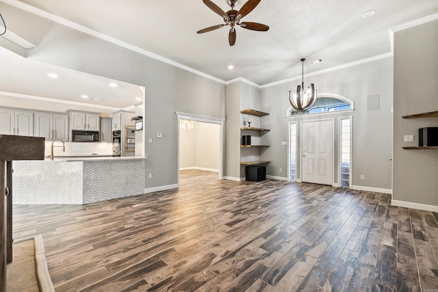 unfurnished living room with ceiling fan with notable chandelier, crown molding, and dark hardwood / wood-style flooring