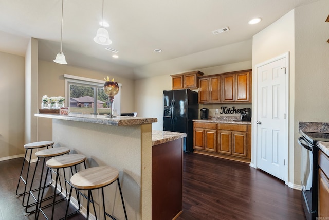 kitchen featuring a breakfast bar area, dark hardwood / wood-style flooring, decorative light fixtures, light stone countertops, and black appliances