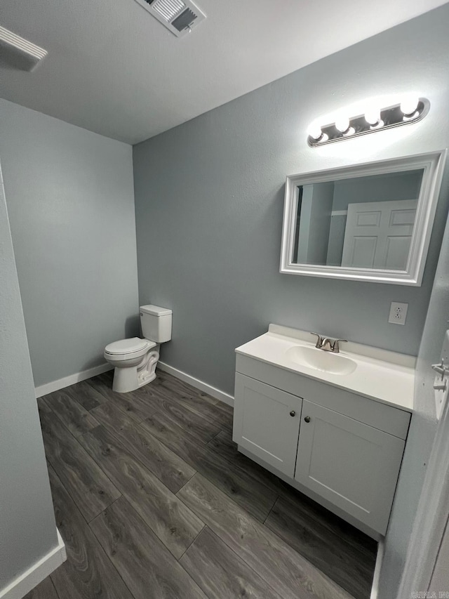 half bath featuring visible vents, baseboards, toilet, wood finished floors, and vanity