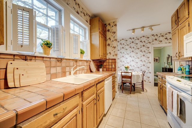 kitchen with sink, light tile patterned floors, white appliances, track lighting, and tile countertops