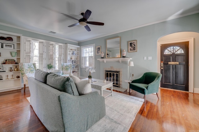 living room featuring wood-type flooring, ornamental molding, and a brick fireplace