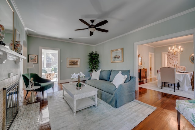 living room featuring ceiling fan with notable chandelier, a brick fireplace, ornamental molding, and wood-type flooring