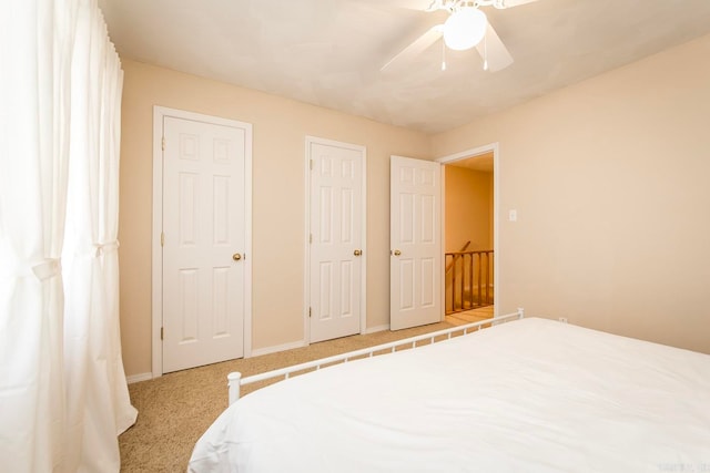 bedroom with two closets, light carpet, and ceiling fan