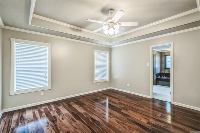 empty room with crown molding, a tray ceiling, dark hardwood / wood-style floors, and ceiling fan