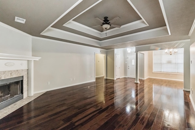 unfurnished living room featuring ceiling fan with notable chandelier, a fireplace, decorative columns, a tray ceiling, and dark hardwood / wood-style floors