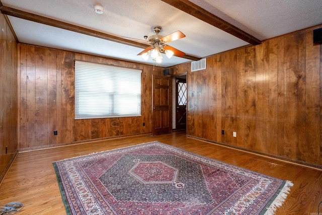 spare room featuring light hardwood / wood-style floors, wood walls, a textured ceiling, and beam ceiling