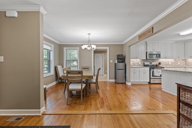 dining room with light hardwood / wood-style floors, crown molding, and an inviting chandelier