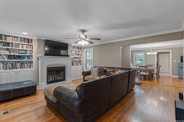 living room with built in features, ornamental molding, ceiling fan with notable chandelier, and light wood-type flooring