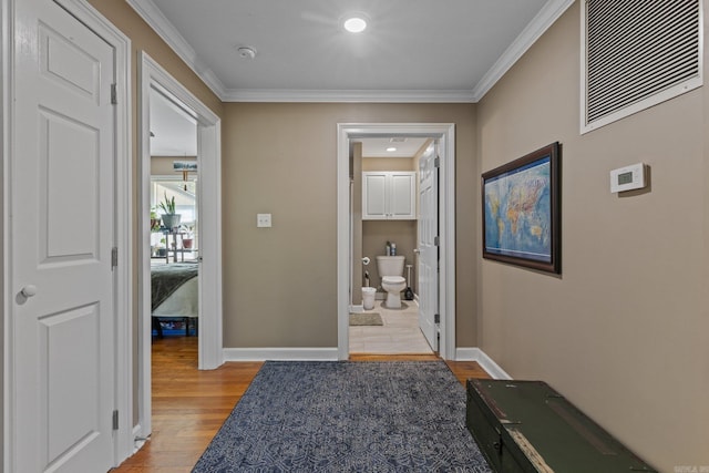 hallway with light wood finished floors, visible vents, baseboards, and ornamental molding