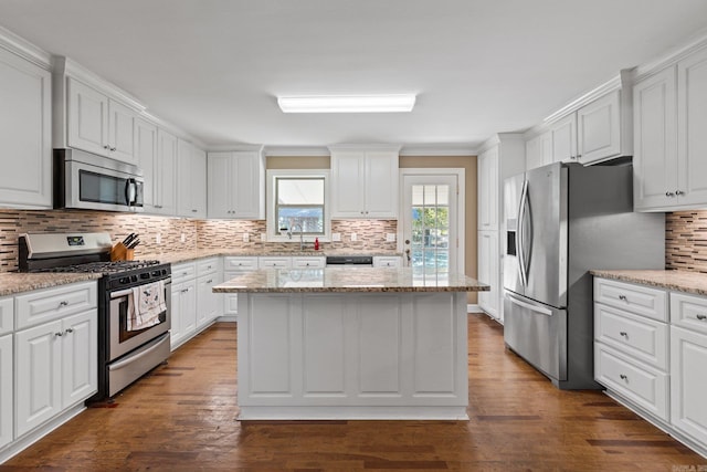 kitchen with a kitchen island, dark wood-type flooring, stainless steel appliances, light stone countertops, and white cabinetry