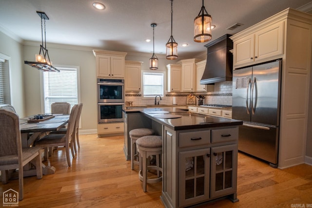 kitchen with a kitchen island, light wood-type flooring, custom range hood, pendant lighting, and stainless steel appliances