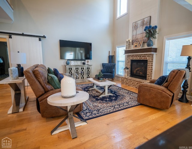 living room with a towering ceiling, wood-type flooring, a brick fireplace, and a barn door