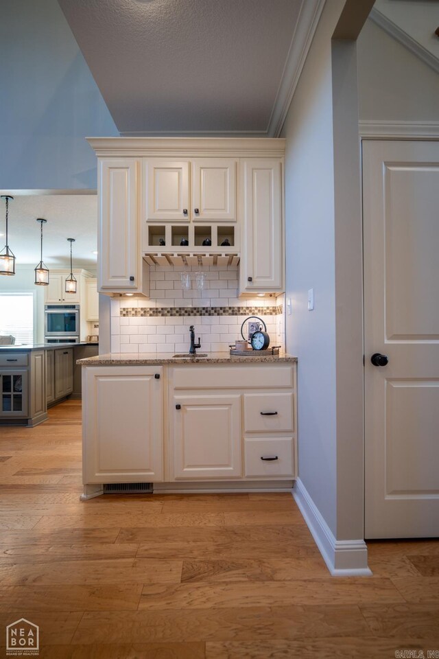 bar with ornamental molding, light stone countertops, light wood-type flooring, and stainless steel oven