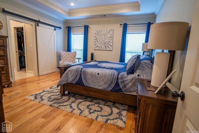 bedroom with crown molding, a barn door, light hardwood / wood-style flooring, and multiple windows