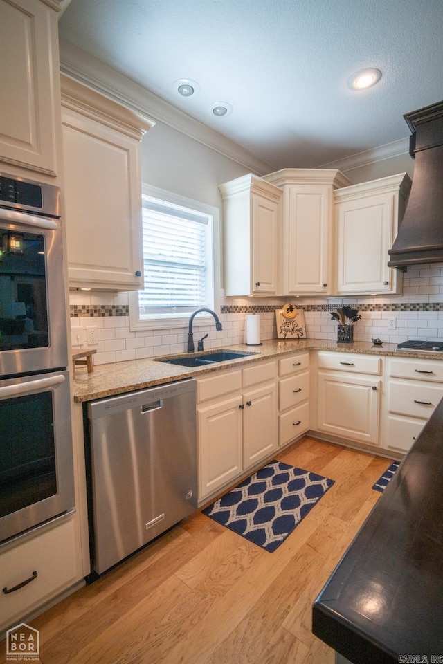 kitchen featuring sink, light hardwood / wood-style floors, stainless steel appliances, custom exhaust hood, and ornamental molding