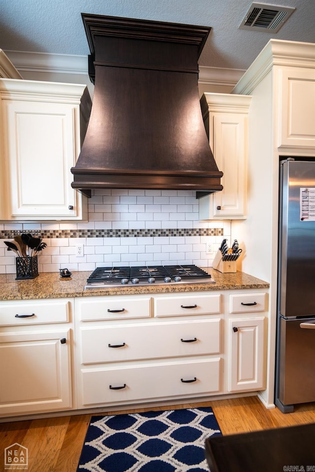 kitchen with custom exhaust hood, decorative backsplash, stainless steel appliances, and light hardwood / wood-style floors