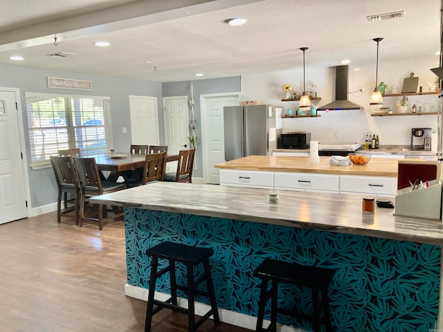 kitchen with wood-type flooring, island exhaust hood, a textured ceiling, pendant lighting, and stainless steel refrigerator