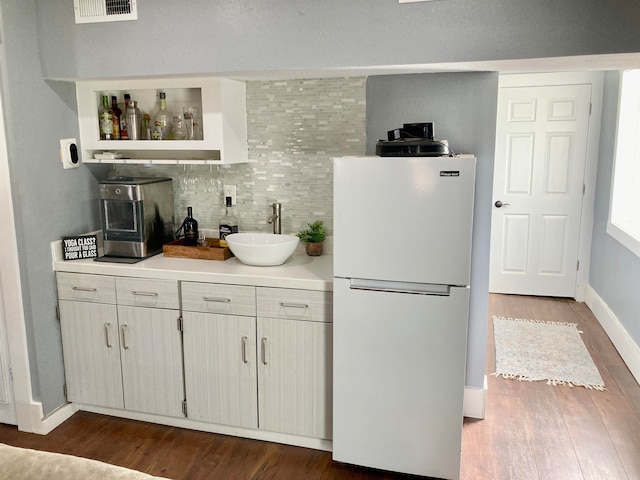 bar featuring white fridge, sink, dark wood-type flooring, and backsplash