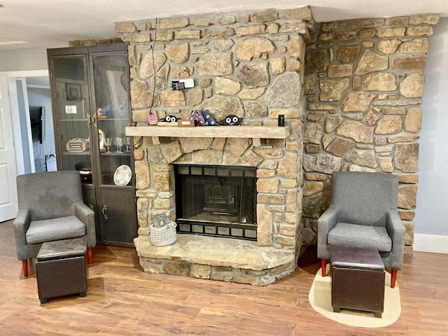 living area featuring a textured ceiling, a stone fireplace, and hardwood / wood-style flooring