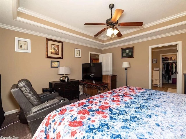 bedroom with a raised ceiling, ceiling fan, crown molding, and a spacious closet