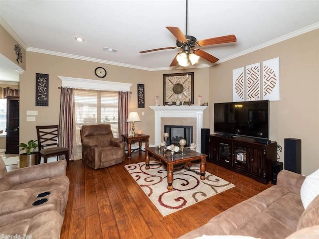 living room with hardwood / wood-style floors, ceiling fan, crown molding, and a tiled fireplace