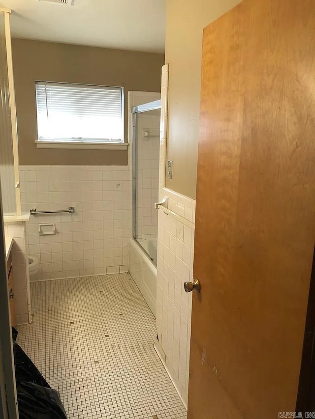 bathroom featuring toilet, tile walls, shower / bath combination with glass door, and tile patterned flooring