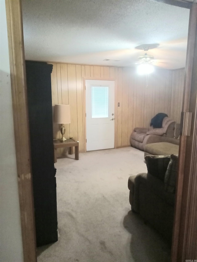 living area with carpet floors, wooden walls, a textured ceiling, and ceiling fan