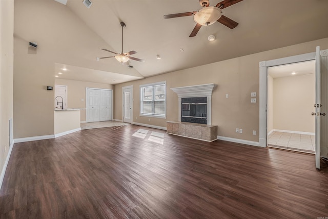 unfurnished living room with ceiling fan, high vaulted ceiling, a tile fireplace, and dark hardwood / wood-style flooring