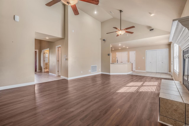 unfurnished living room featuring light hardwood / wood-style flooring, a tiled fireplace, high vaulted ceiling, and ceiling fan