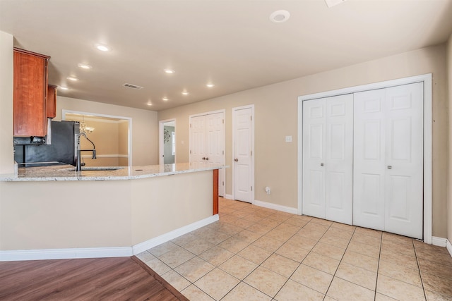 kitchen with kitchen peninsula, light stone countertops, light hardwood / wood-style flooring, fridge, and sink