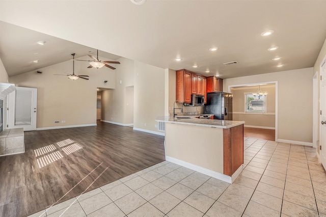 kitchen featuring lofted ceiling, a tiled fireplace, black fridge, kitchen peninsula, and light wood-type flooring