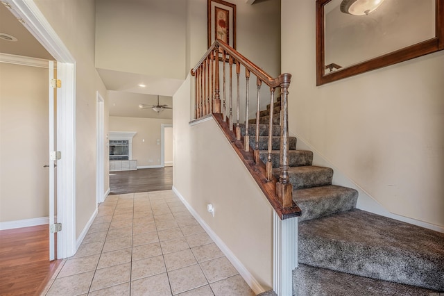 stairway featuring ceiling fan, a high ceiling, a fireplace, and hardwood / wood-style floors