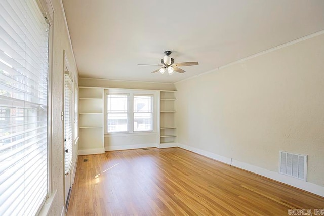 spare room featuring built in shelves, ceiling fan, crown molding, and light wood-type flooring