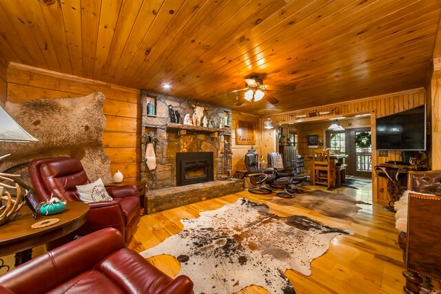 living room featuring a stone fireplace, hardwood / wood-style flooring, wooden walls, and ceiling fan