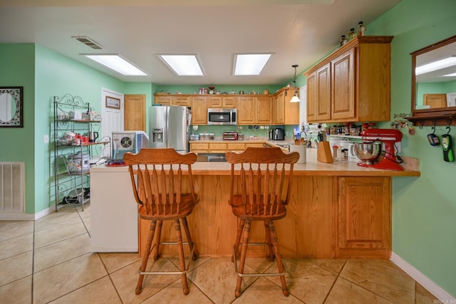 kitchen with light tile patterned floors, appliances with stainless steel finishes, a breakfast bar area, and kitchen peninsula