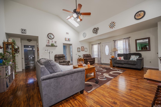 living room with ceiling fan, high vaulted ceiling, a skylight, and dark hardwood / wood-style flooring