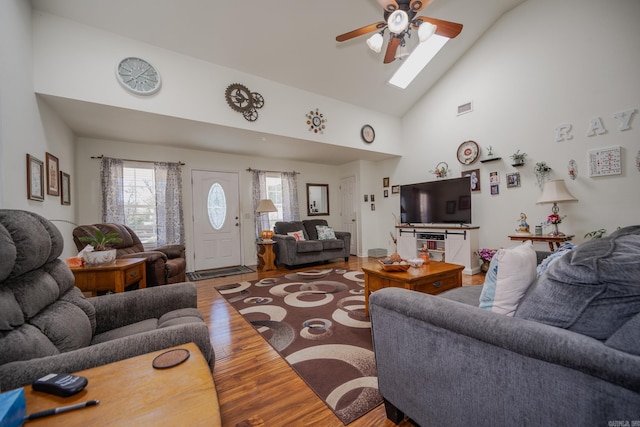 living room featuring hardwood / wood-style floors, ceiling fan, high vaulted ceiling, and a skylight