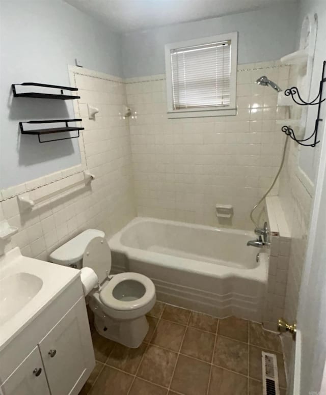 full bathroom with tiled shower / bath, tile walls, vanity, toilet, and tile patterned floors